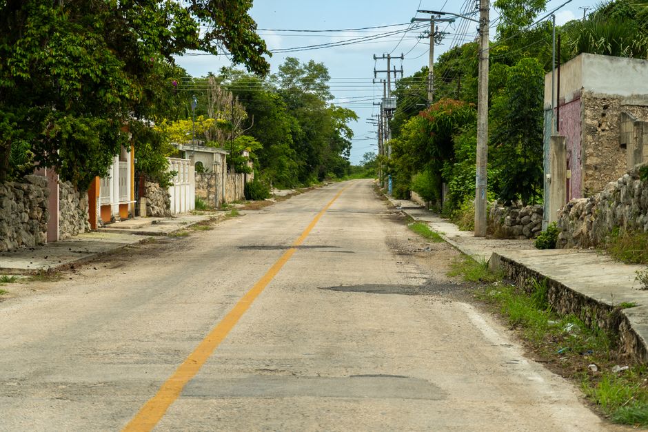Quiet rural street in Suma, Yucatán, surrounded by lush greenery and rustic architecture.