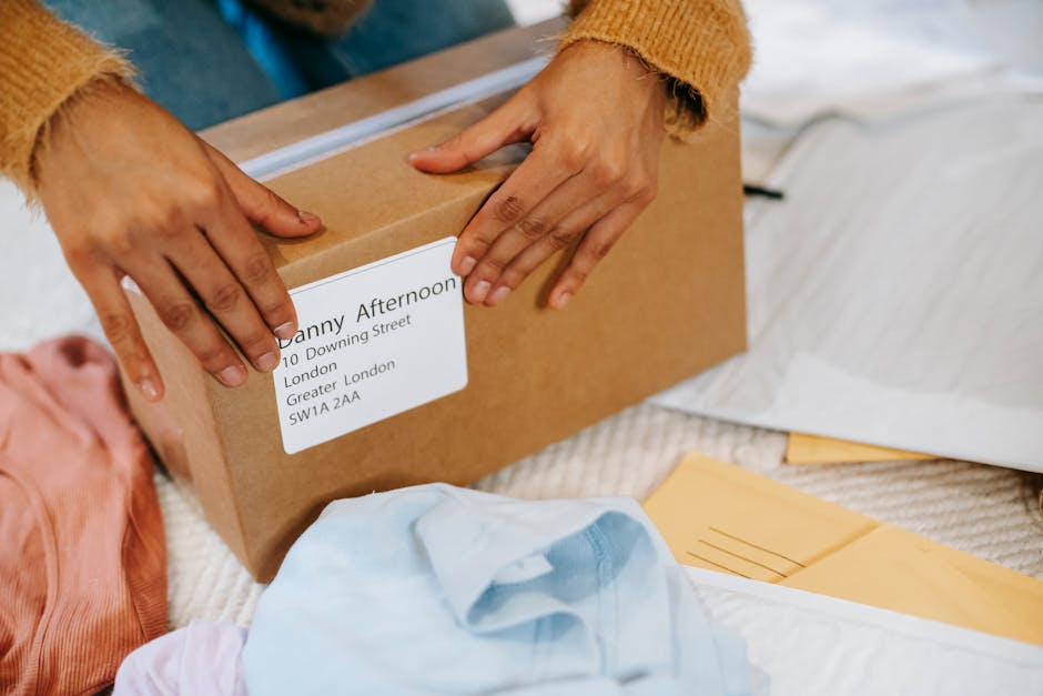 From above of crop anonymous female packing carton box with parcel among envelops and clothes