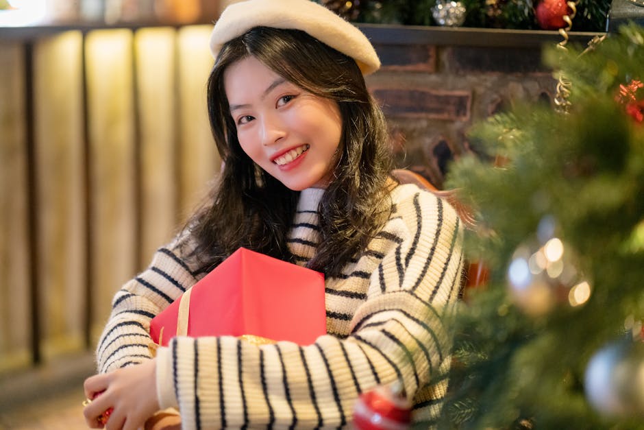 A cheerful woman in winter attire holding a gift, surrounded by festive holiday decorations indoors.