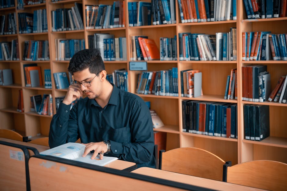 A young man engaged in study within a library filled with books. Ideal for educational themes.