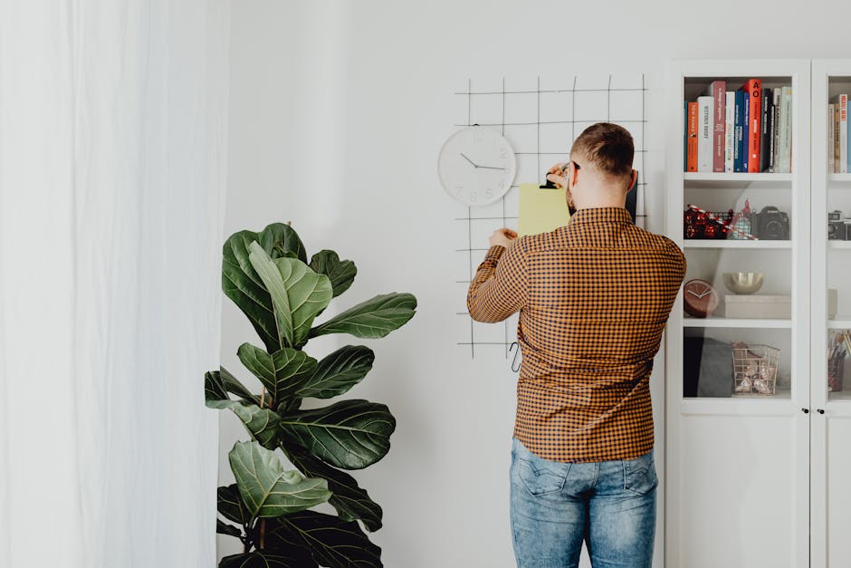 A man posts a note on a grid wall, indicating a reminder or schedule update in a modern home office environment.