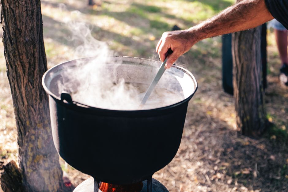 A person stirring a steaming pot outdoors, showcasing rustic cooking methods.