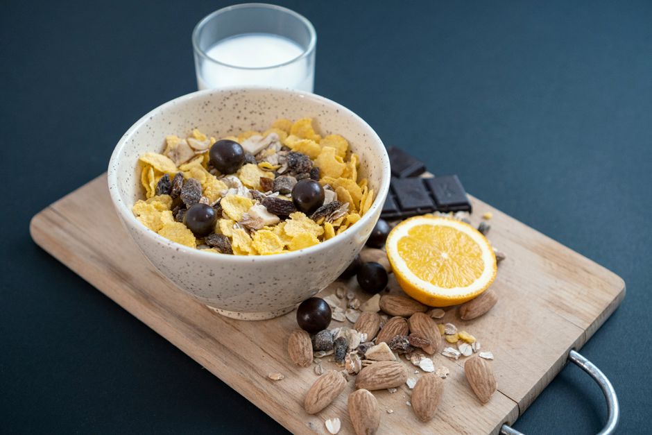 A bowl of granola with almonds, dried fruit, and milk on a cutting board for a healthy breakfast.