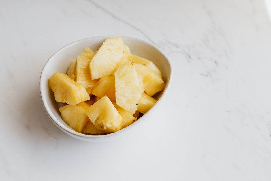 From above of fresh ripe sliced pineapple in white porcelain bowl placed on marble table
