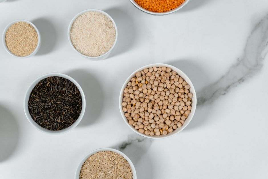 Top view of assorted grains and lentils in white bowls on a marble surface for culinary concepts.