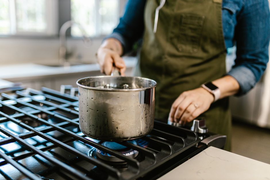 A woman in an apron cooking with a pot on a gas stove, embodying a cozy domestic kitchen scene.