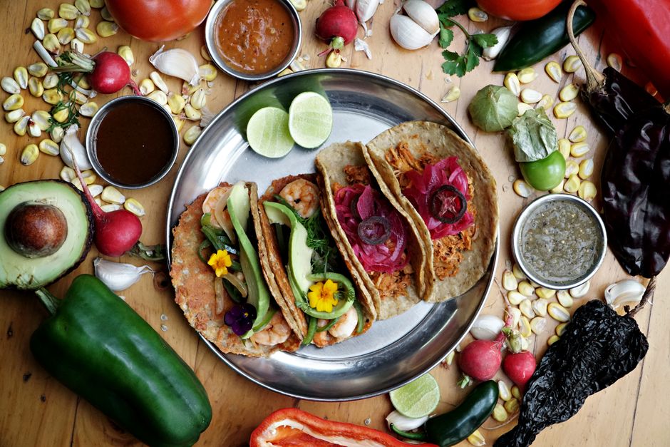 Vibrant Mexican tacos on a platter with fresh vegetables and spices, showcasing traditional culinary art.