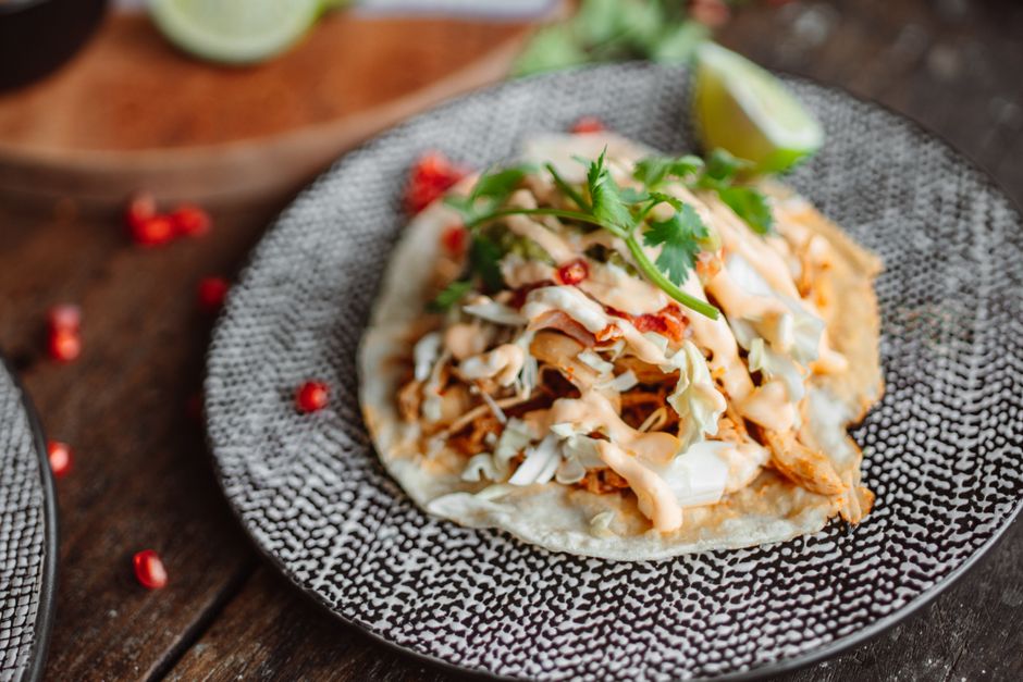 Close-up of a tasty chicken taco topped with cilantro and lime on a rustic plate.