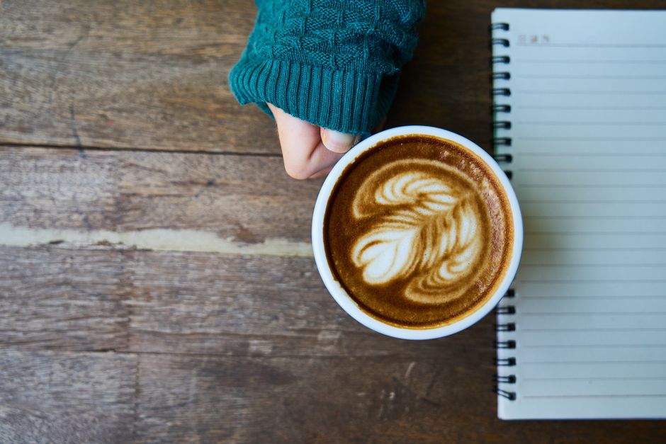 Overhead shot of a latte with art next to an open notebook on a rustic wooden table.