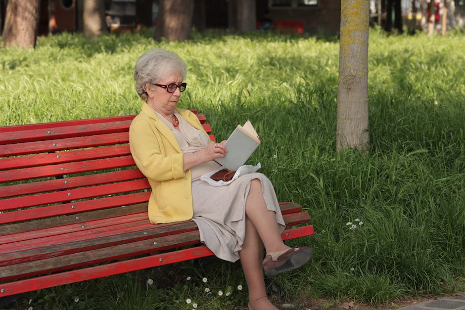 Elderly woman reading a book on a red bench in a serene Venice park setting.