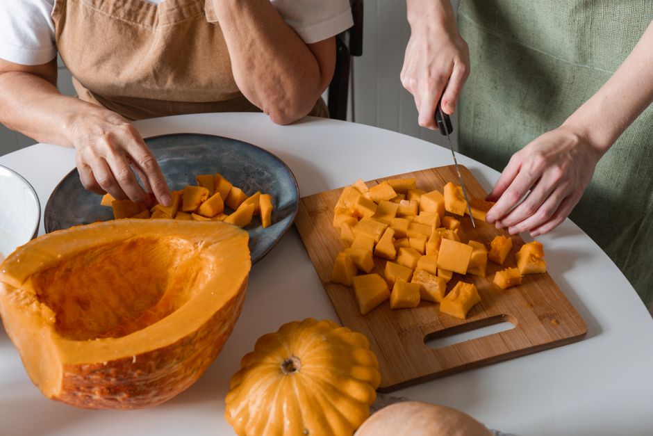 Two people cutting pumpkin cubes on a wooden board, engaging in food preparation.