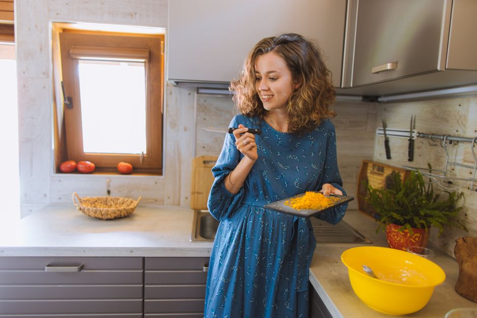 Smiling woman preparing food in the kitchen, holding a knife and cutting board.