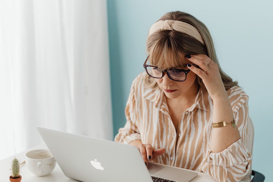 A woman in a cozy home office environment, appearing frustrated while working on a laptop.