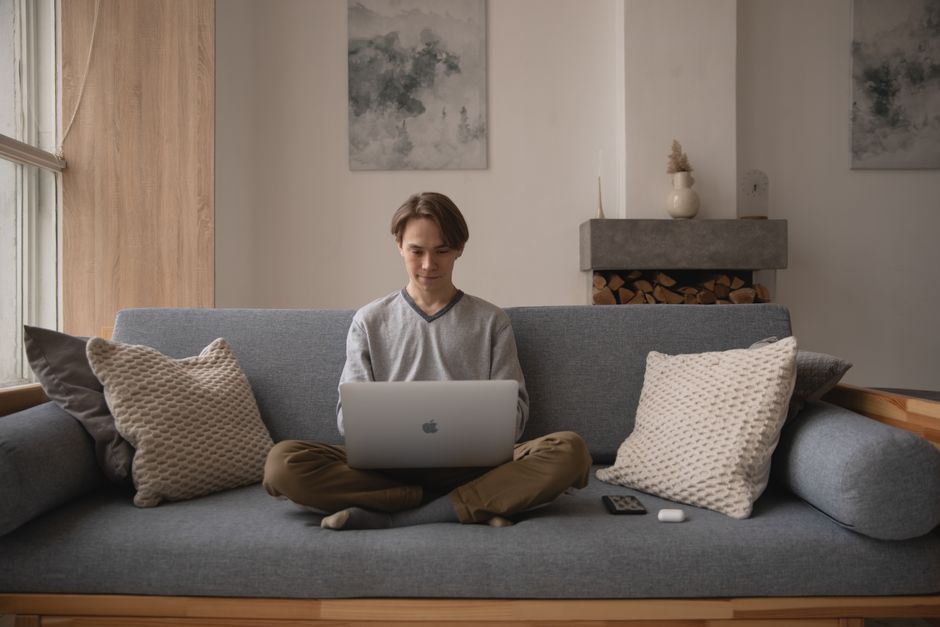 Man sitting on a couch using a laptop in a cozy home setting, remote working.