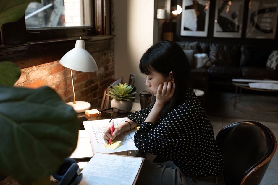 Asian woman engaged in remote work at a home office desk with documents.